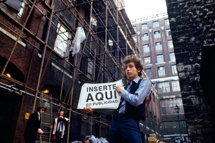 Bob Dylan en la calle muestra una pancarta publicitaria.