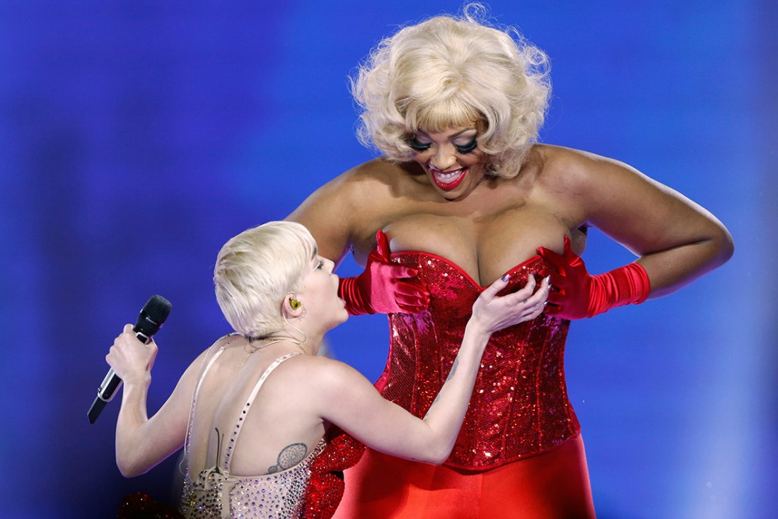 Miley Cyrus toca los pechos a una mujer vestida de rojo.