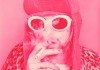 Kurt Cobain con gafas de sol blancas, un gorro y fumando, con un filtro rosa