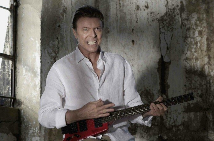 David Bowie tocando una guitarra sin clavijero en una casa en ruinas