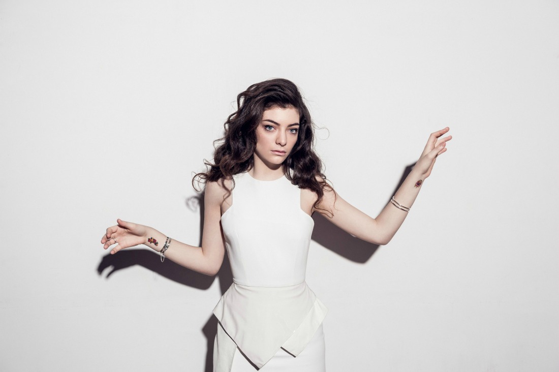 Lorde con vestido blanco y las manos alzadas.