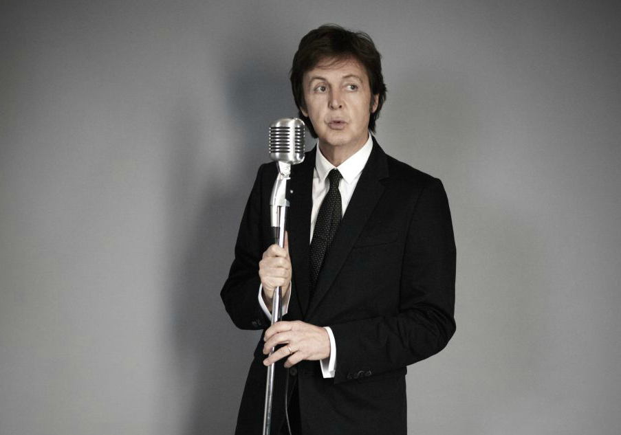 Paul McCartney con un micrófono en una pared gris