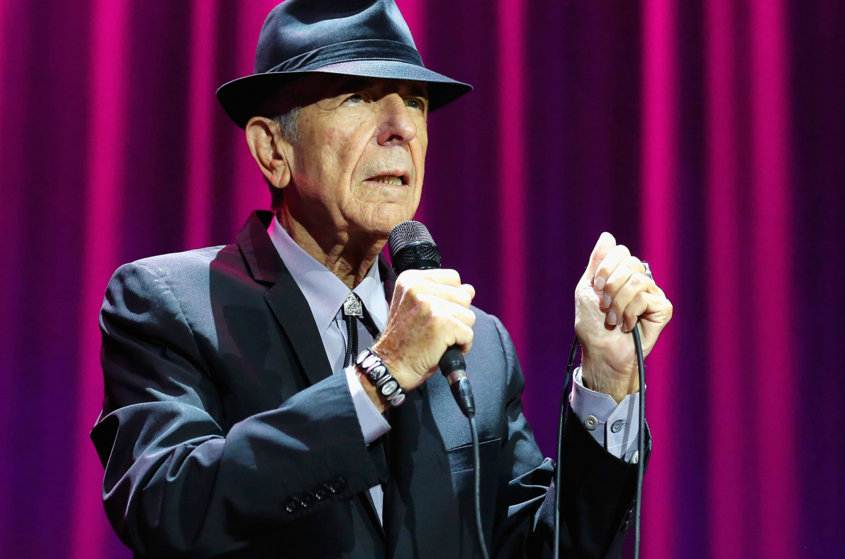 Leonard Cohen con un micrófono frente a un telón morado