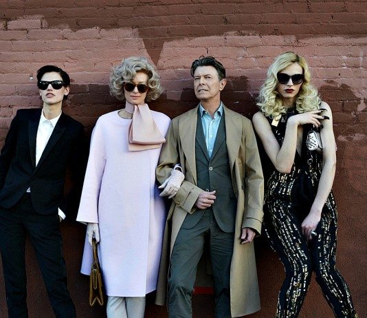 David Bowie junto a tres mujeres en una pared roja.